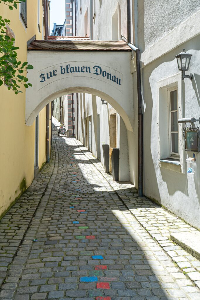 Painted cobblestones and the Zur blauen Donau archway in Passau's Höllgasse